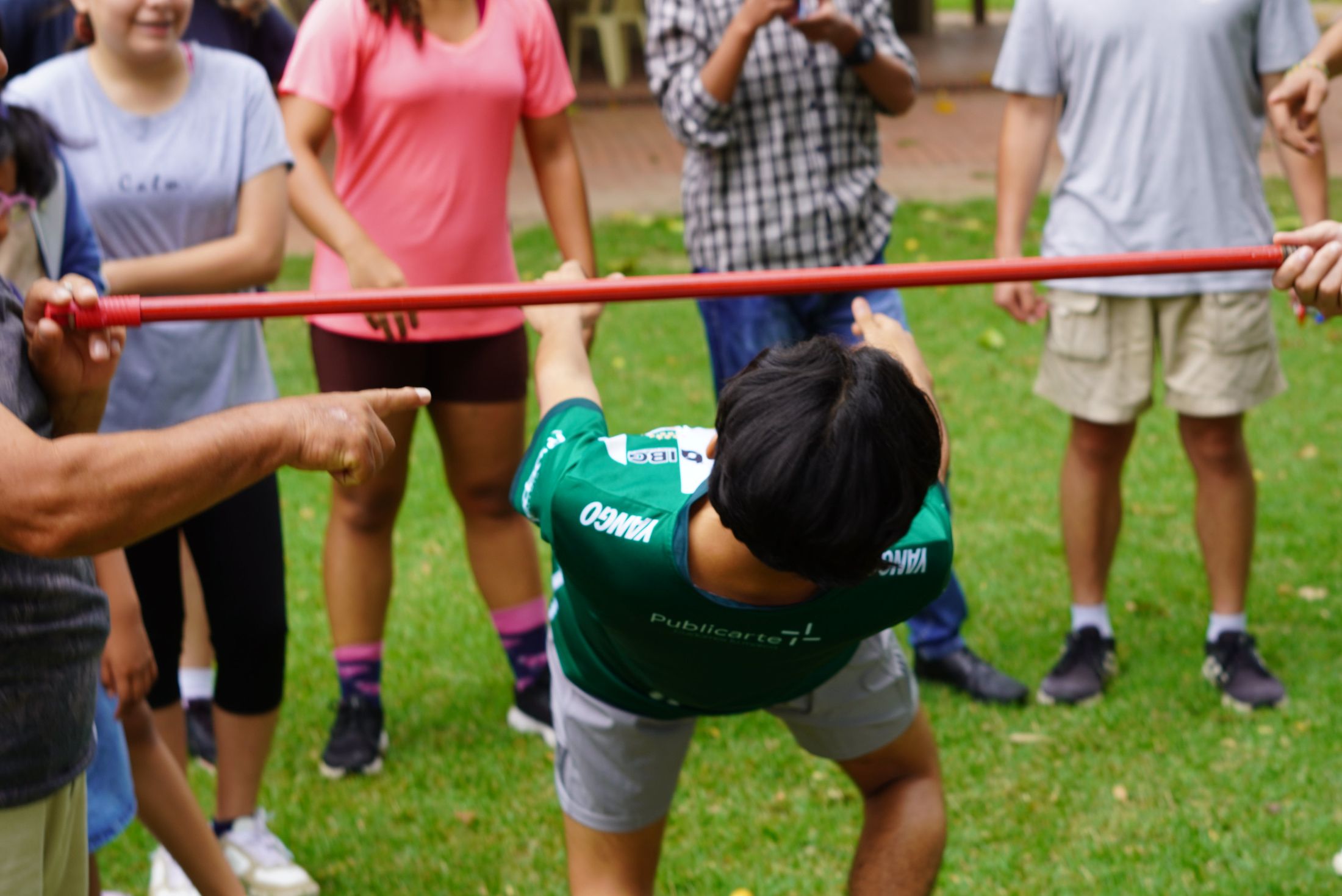 A camper bending backwards under a limbo pole while friends point and cheer
