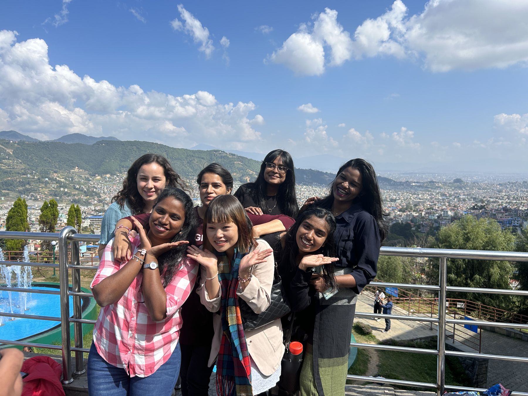 Seven young women from the Swamp Corps team at a railing above the Kathmandu valley