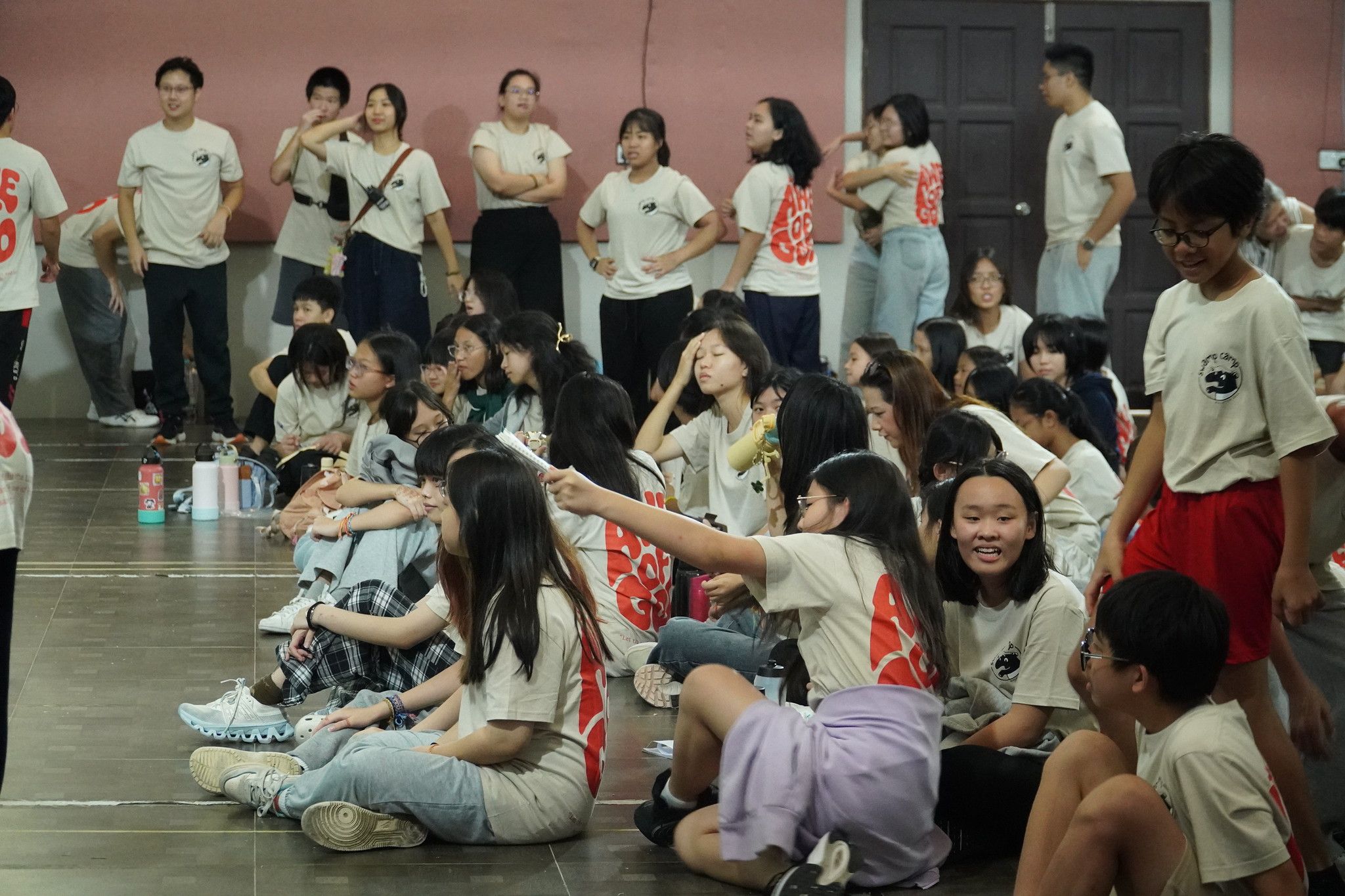 Campers in matching shirts seated together on the hall floor at Swamp Camp Malaysia