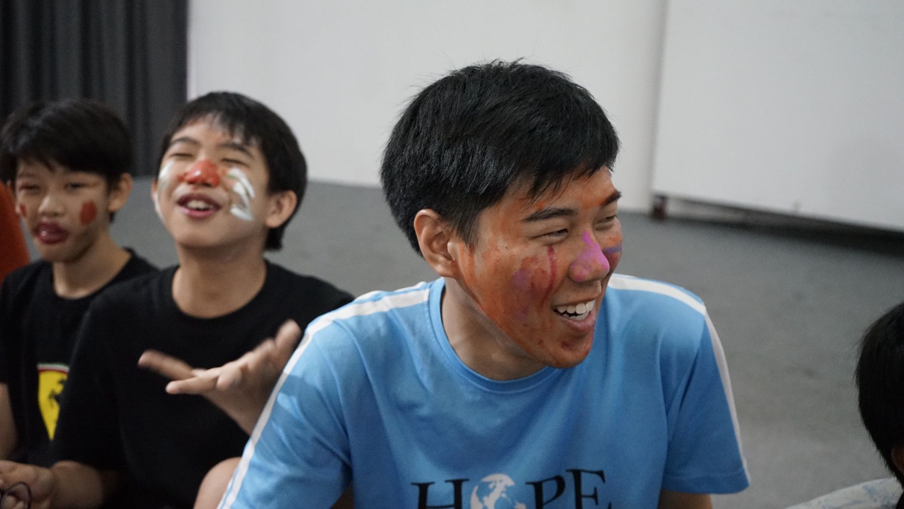 A counselor laughing with his face painted, campers laughing behind him
