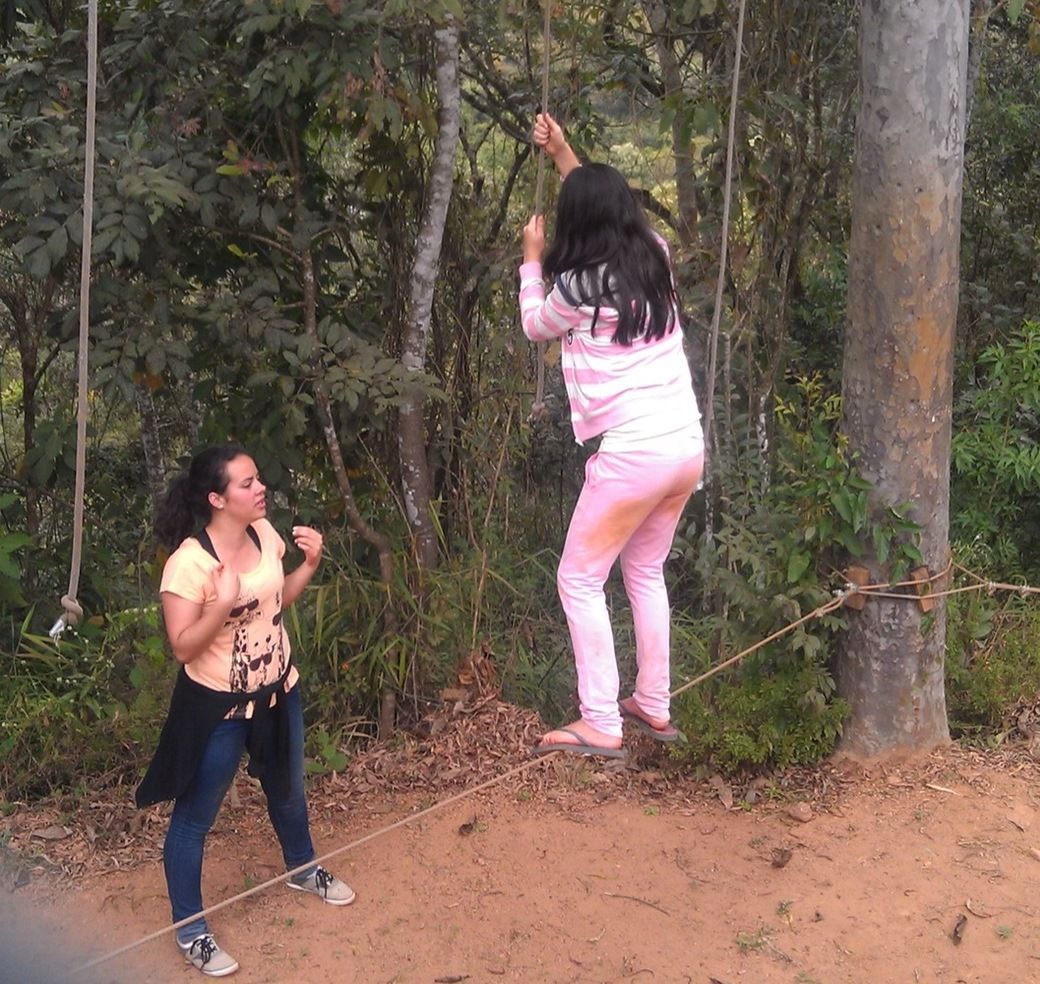 A young camper balancing on a low rope between trees while a friend spots her